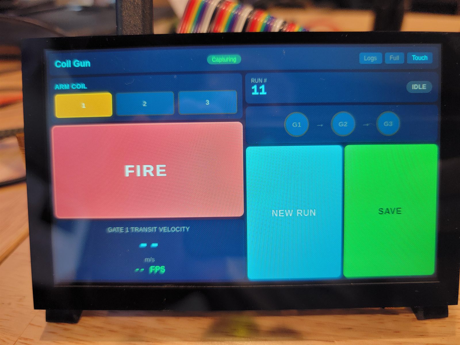 Touchscreen controller showing the coil gun interface: arm coil selector, a large FIRE button, run number 11, a gate chain G1 to G2 to G3, and a Gate 1 Transit Velocity field reading two dashes instead of a number.