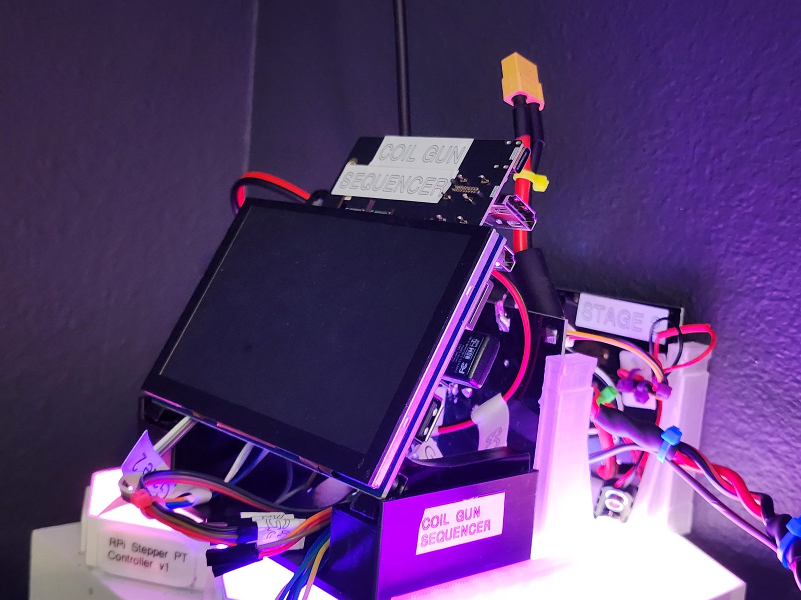 Black 3D-printed enclosure labelled COIL GUN SEQUENCER holding a Raspberry Pi, a driver shield and a touchscreen, with an XT60 power lead, lit magenta.