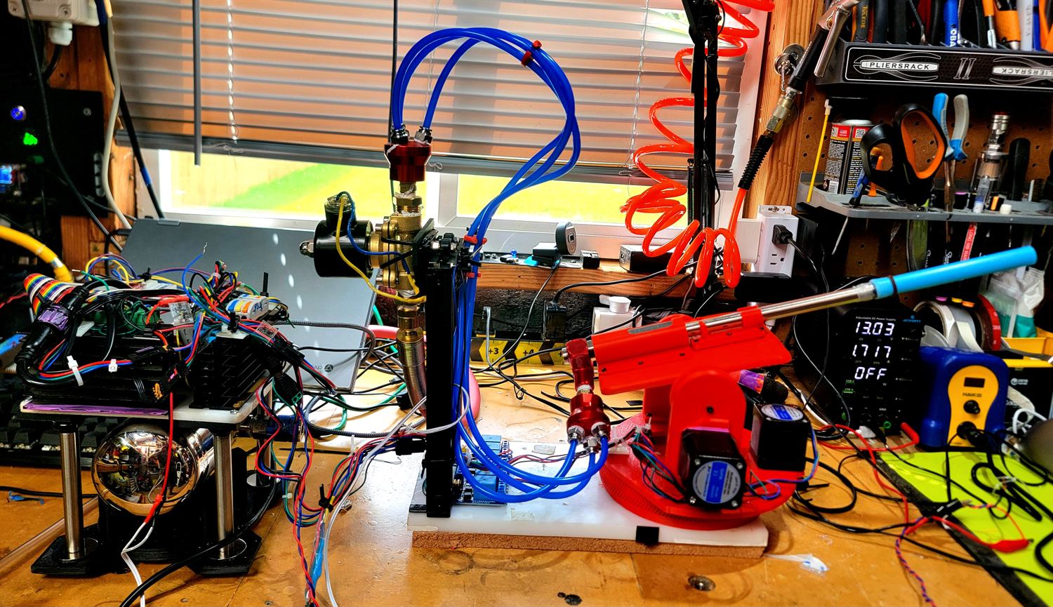 Bench integration: the red turret beside a vertical pneumatic column with brass manifold and blue tubing, wired to a heatsinked stepper driver stack.